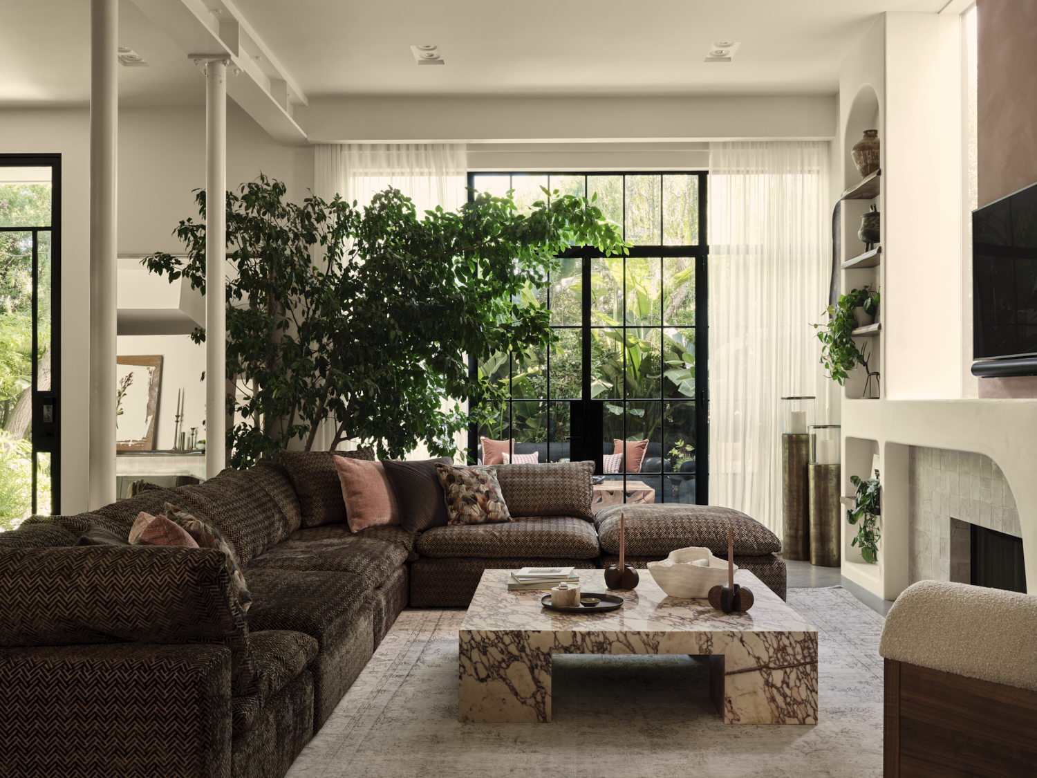 A living room with a brown sofa, a marble coffee table and large tree