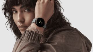 En kvinna sitter med armen vid ansiktet, med en Google Pixel Watch med ett ljusgrått band runt handleden.