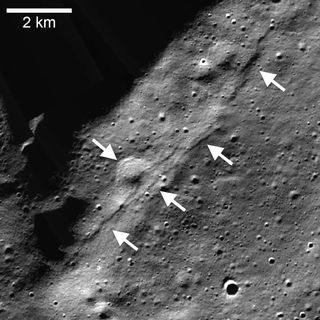 A view of the gray lunar surface with a fault line running diagonally starting in the top right and ending in the bottom left of the image. Arrows indicate the fault line.