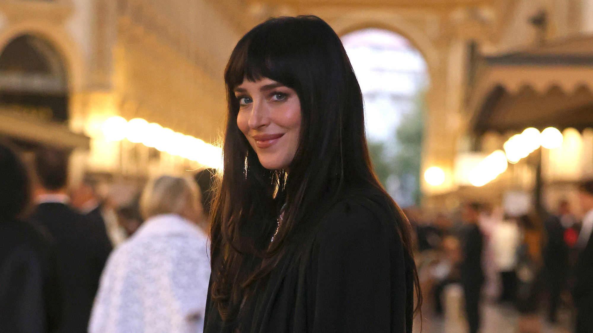 Dakota Johnson in black Verity-adjacent open blouse at Paris Fashion Week event. 