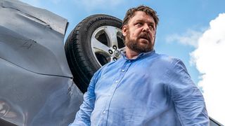 Russell Crowe as Tom Cooper looking unkempt next to an overturned car in Unhinged.