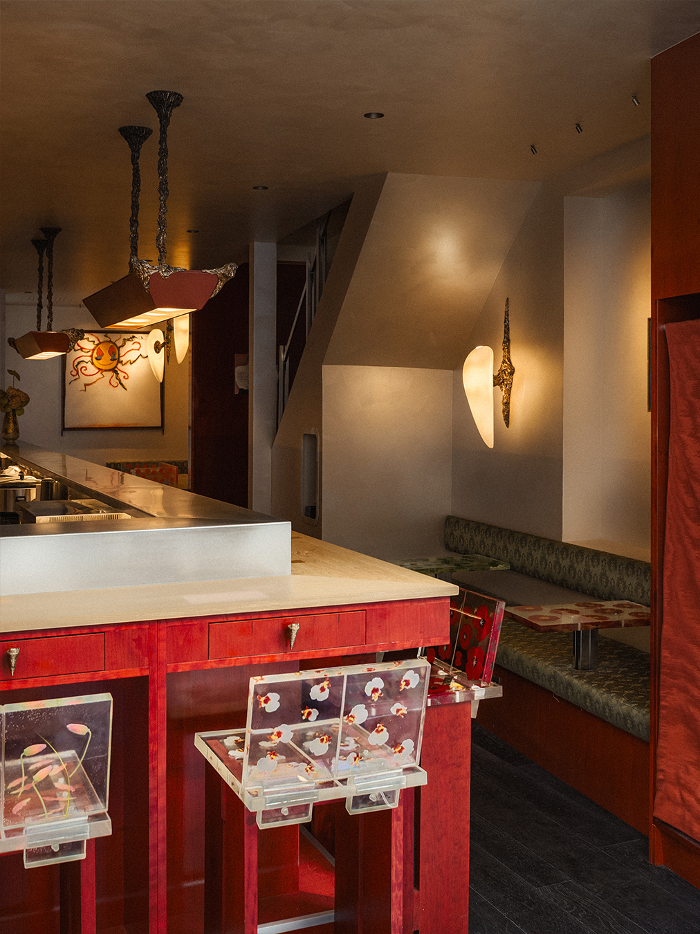 A red-painted wood and chrome bar of a restaurant, decorated with tall, geometrically cut wooden stools with flower-decorated resin backs.