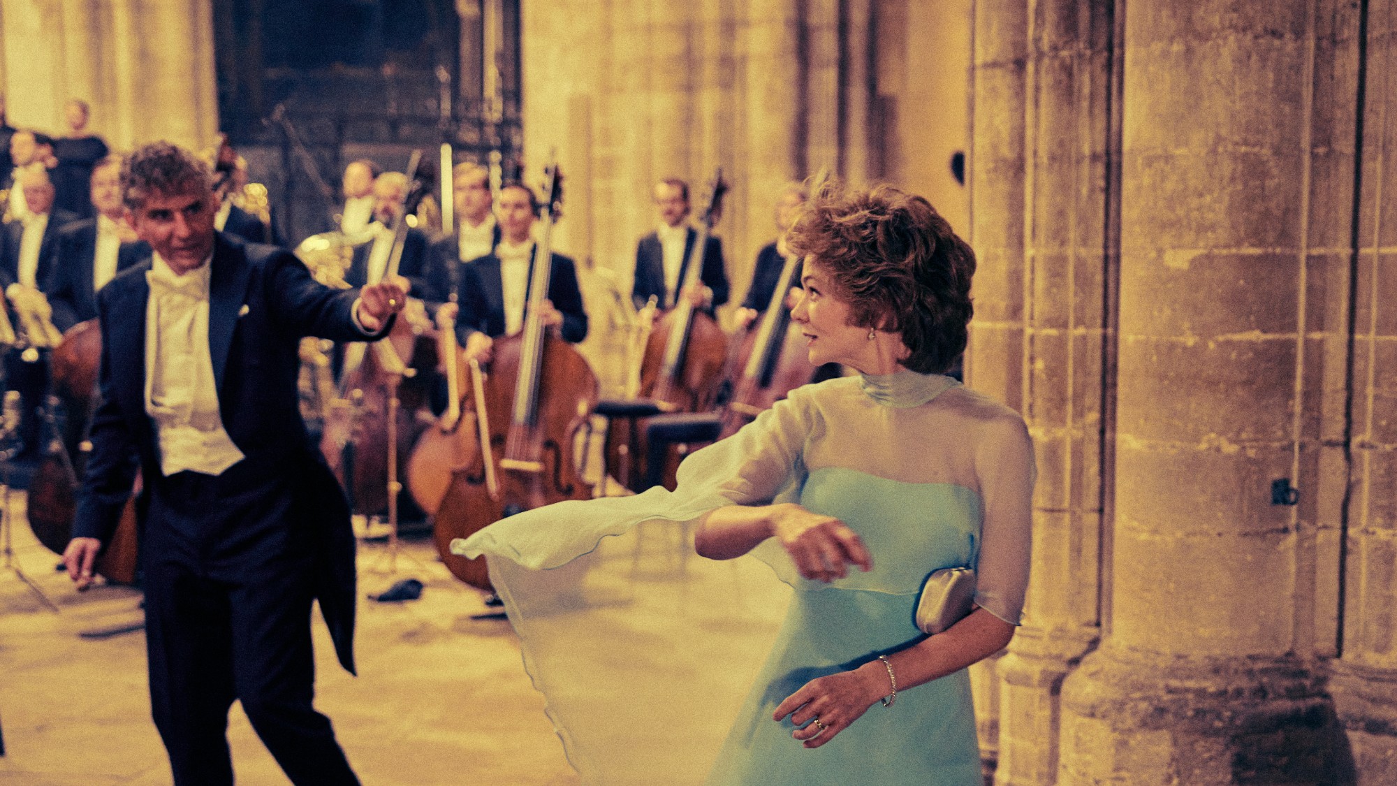 sepia-toned image of Carey Mulligan and Bradley Cooper in a still from the movie Maestro. she is in a light-blue flowing gown; he is in a tuxedo. 