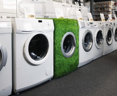 white washing machines lined up on the sales floor with one covered in fake grass. 