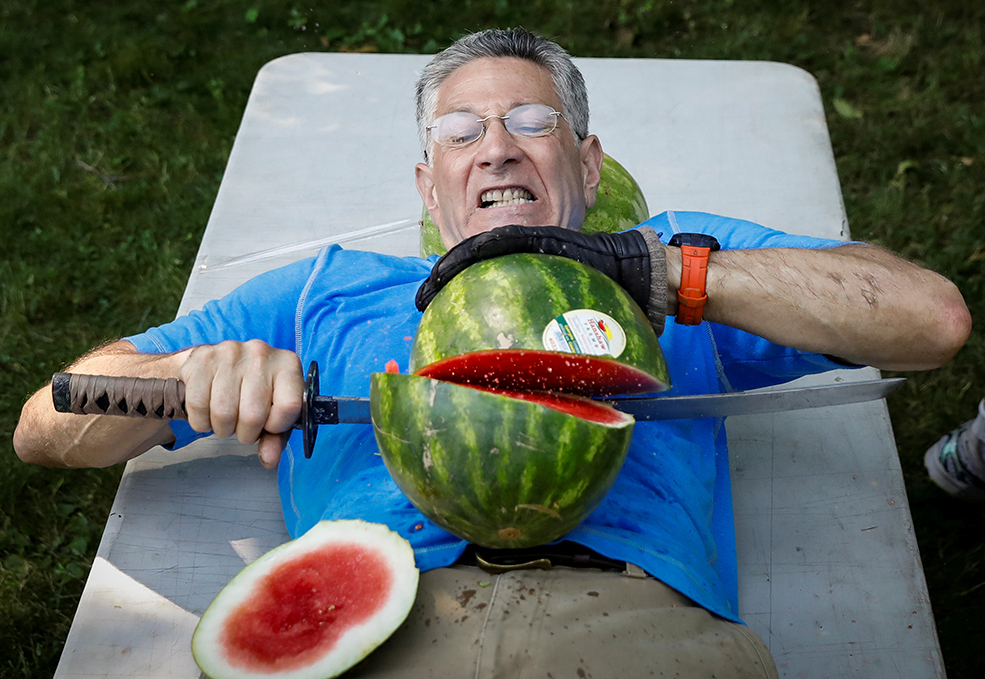 A man slicing watermelons on his stomach.