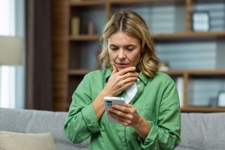 Worried senior woman mother sitting on sofa at home and holding phone.