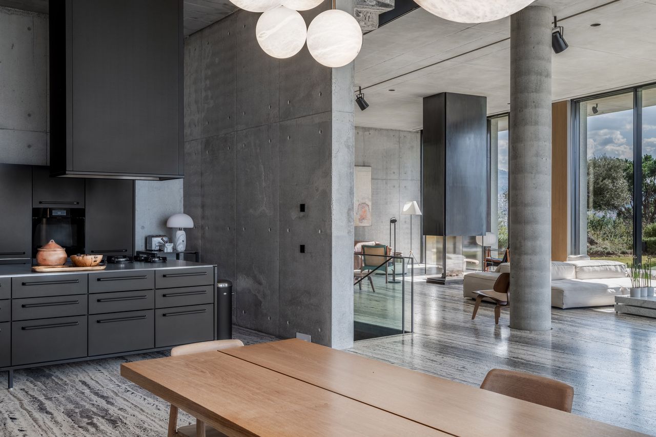 An open place space with a black themed kitchen leading on to a minimalist living room