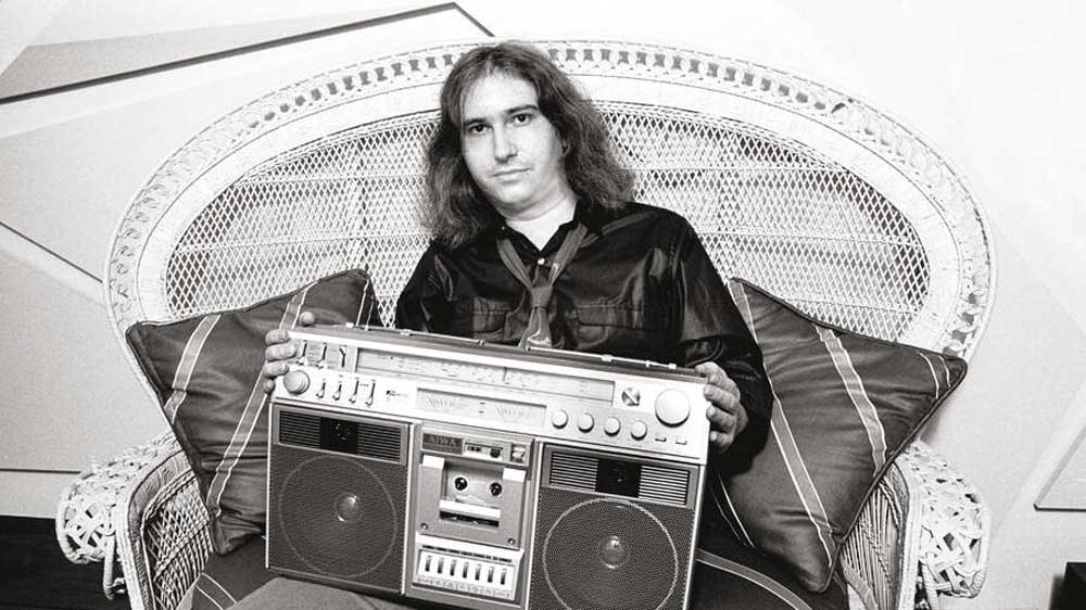 Portrait of American Rock composer, musician, and producer Jim Steinman (1947 - 2021), sitting in a large wicker chair, as he holds a boom box on his lap, New York, New York, April 30, 1981. 