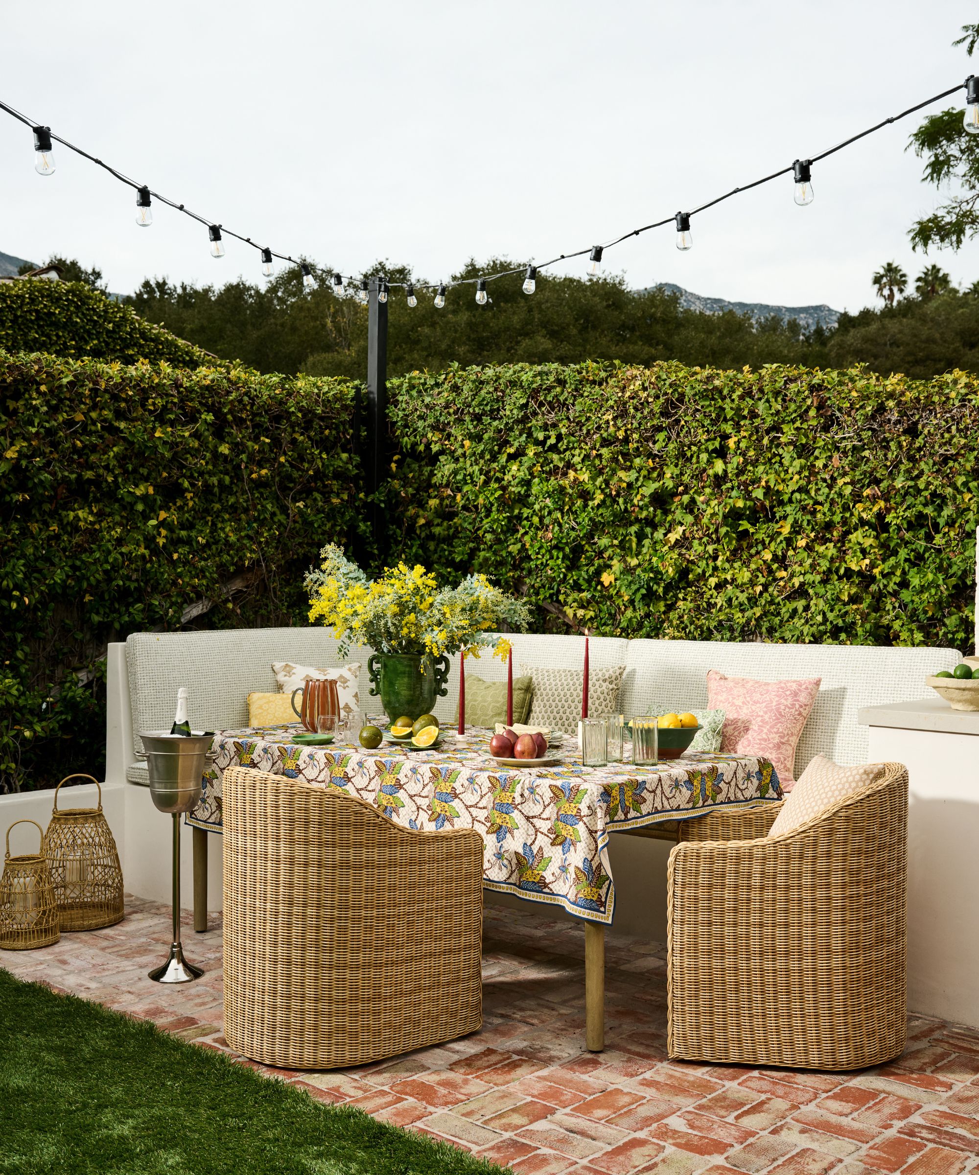 a playful cottage backyard with hedge border, a banquette seat, wicker tub chairs and a table laid for summer dining