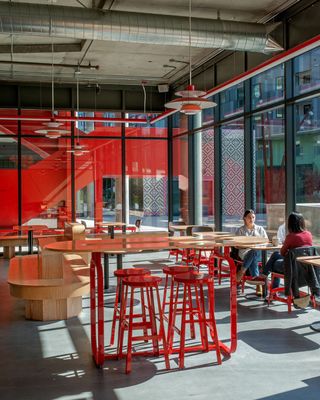 The retro-futuristic interiors of a coffee shop feature 60s-inspired sculptural lighting in red, red metallic stools, futuristically conceived wooden tables, seats, and coffee tables.