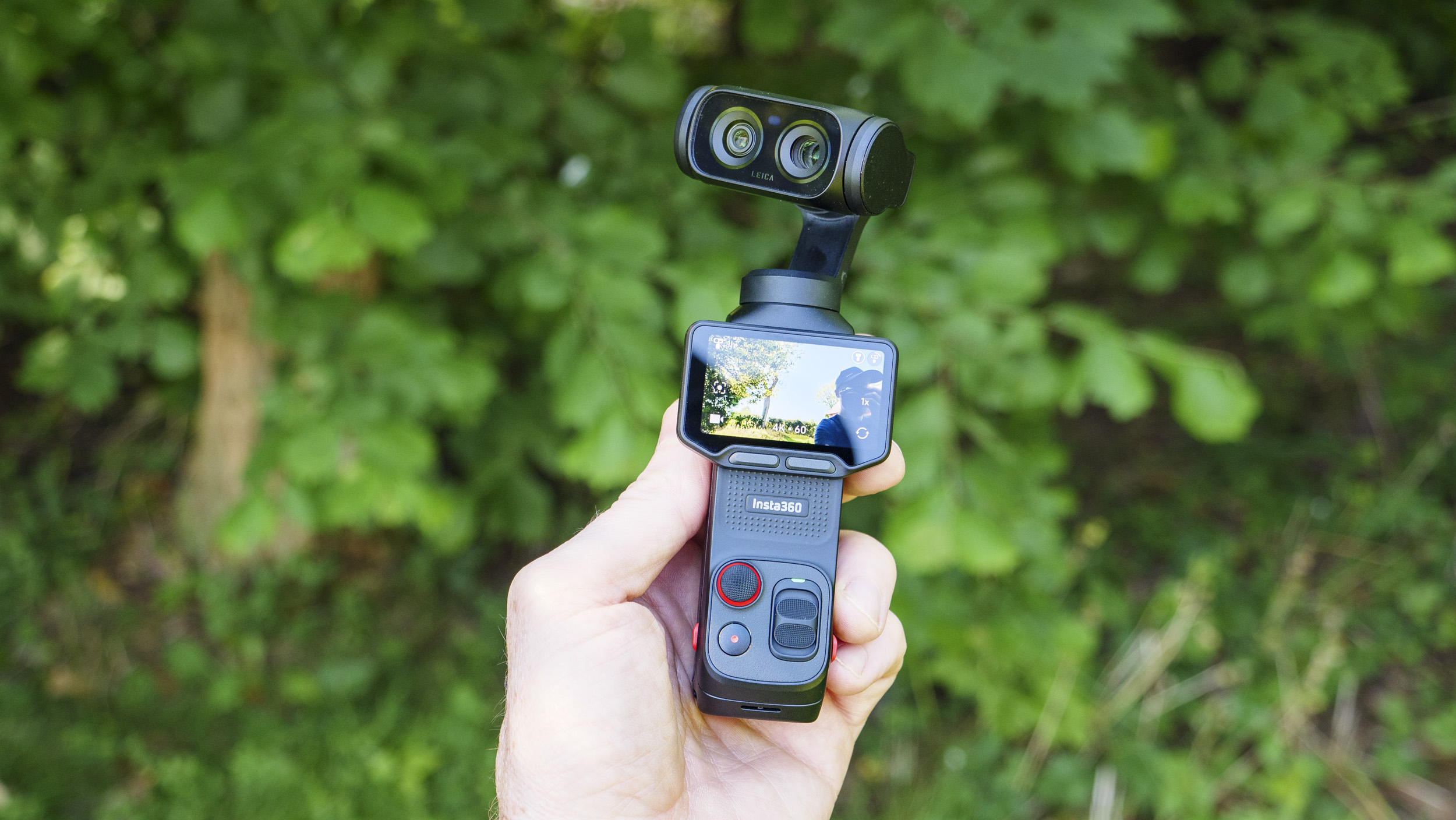 Insta360 Luna Ultra vlogging camera in person's hand, dual-lens pointed back, leafy background