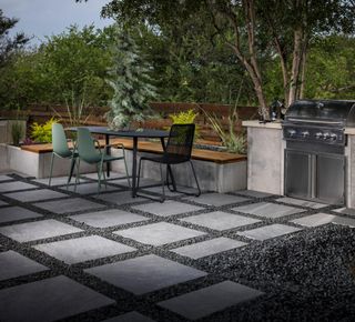 Gray patio pavers interspersed with gravel with black patio dining table and chair, with sage green chair accents and a large built in bbq