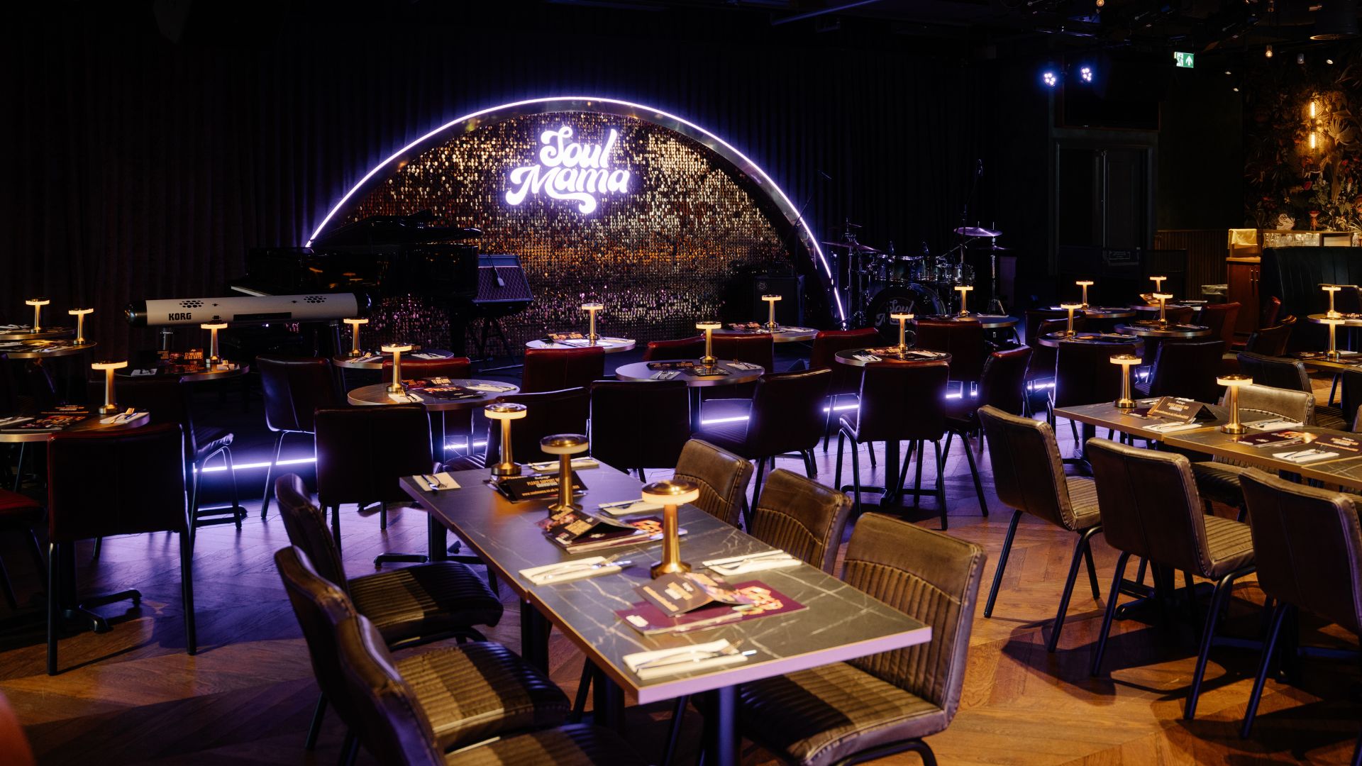 an image of the interior of Soul Mama Islington, showing the trademark purple and gold stage with neon lighting at the back, and plenty of long tables in the space 