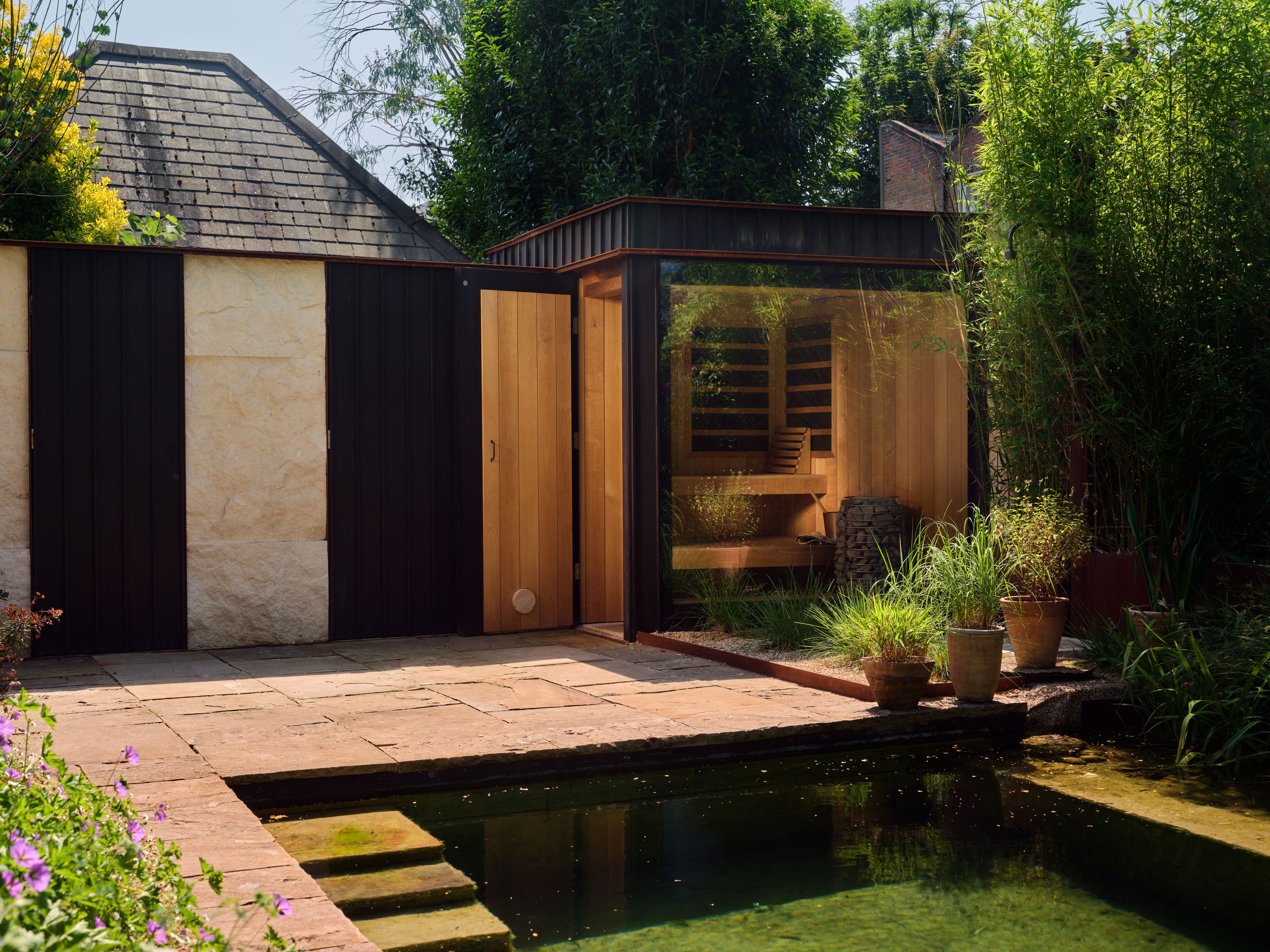 London garden with a natural pool and a wooden sauna behind it