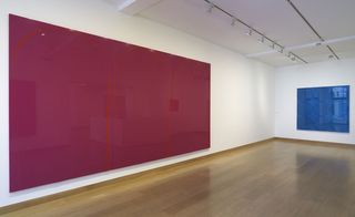 A gallery with a large pink painting on one wall and a square blue one on the other wall.