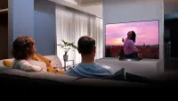 LG BX OLED lit up in a living room with a couple on the sofa watching it