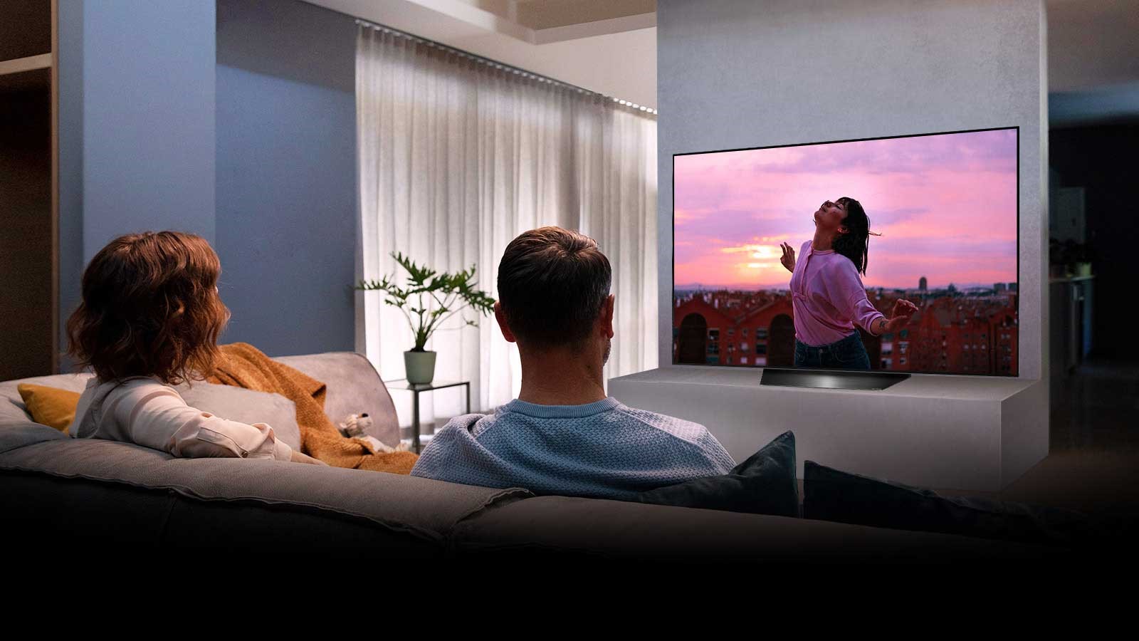 LG BX Series OLED on a TV stand in a cosy living room while a couple watch it