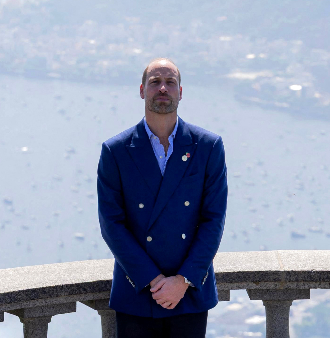 Prince William wearing a blue blazer standing in front of a railing over the sea in Brazil