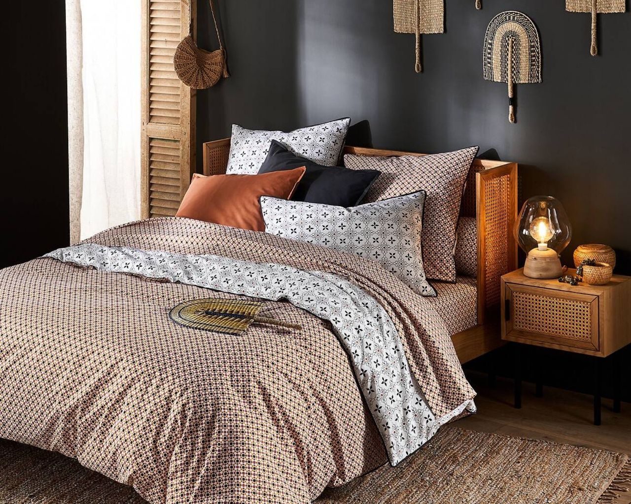 Rattan bed frame inside black room with jute rug and other rattan furniture and decorative patterned bedding