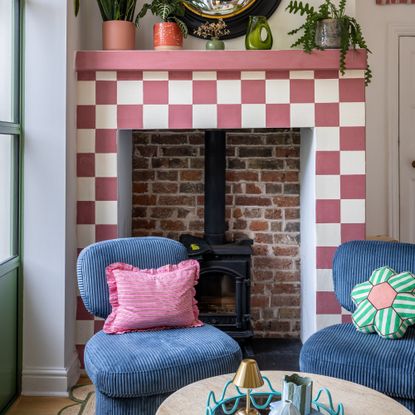 A living room with a fireplace painted in a pink and white chequered pattern and two blue corduroy accent chairs from MADE