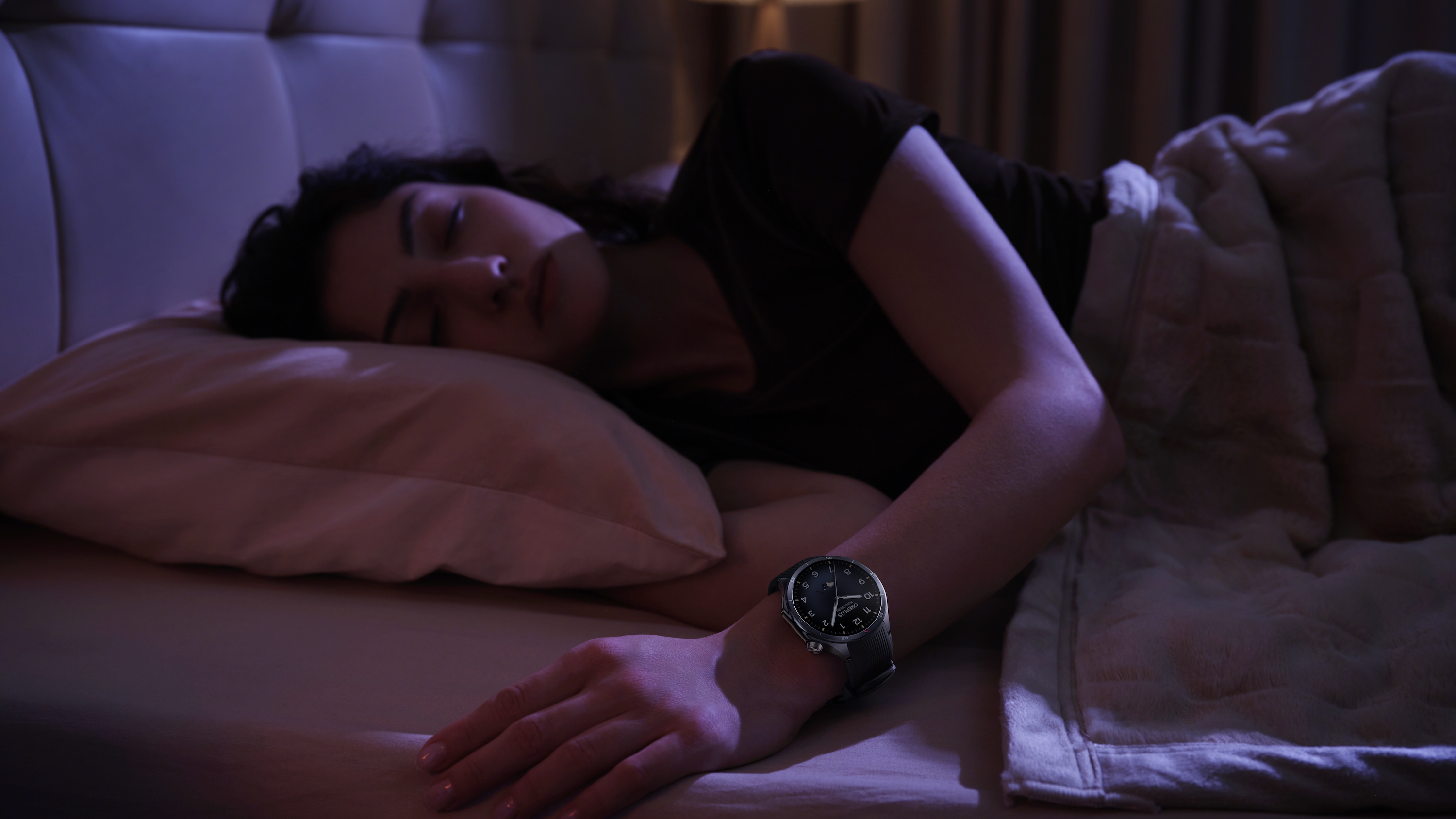 A sleeping woman laying in bed in a dark room wearing a OnePlus Watch 3.