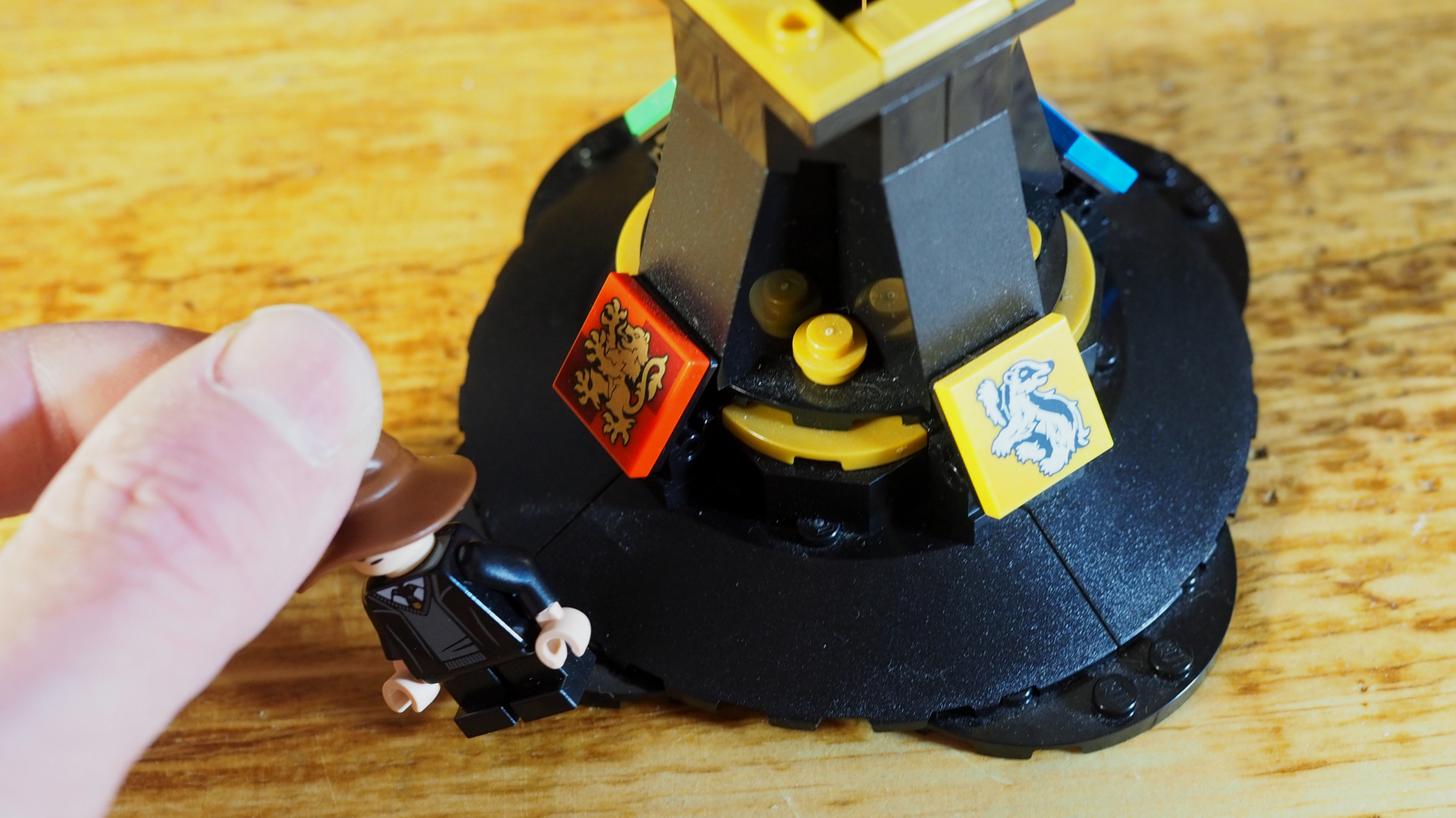 A hand places a Harry Potter minifigure wearing a tiny Sorting Hat onto a stand with Hogwarts House plaques