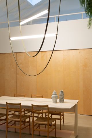 Interior view of the dining area at the Formafantasma Milan studio featuring a light coloured dining table with items on top, wooden chairs and the ‘Wireline’ chandelier