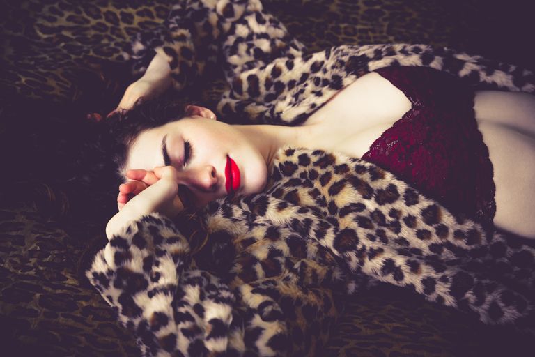 Glamour and red lipstick: dreamy woman on bed. Dreamy and sensual woman has a retro pinup style and is wearing leopard print. Woman is tired and sleepy and her eyes are closed, best bralettes