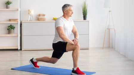 Older man at home lunging on a yoga mat
