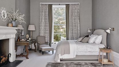 A grey bedroom with a double bed, mantel, window, large curtains