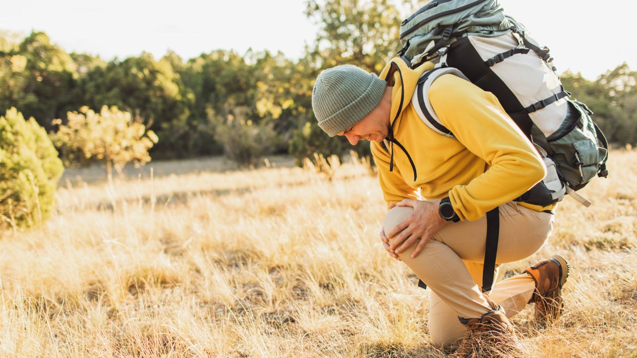 A man holding his knee in pain whilst on a hike