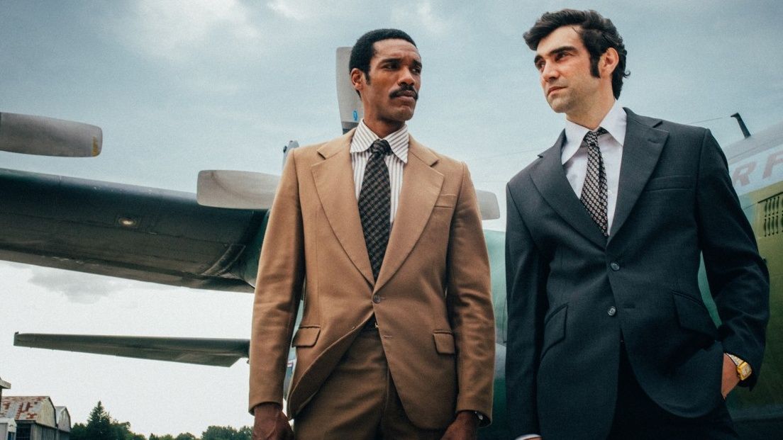 Frank Jackson (played by Peter Sawyers) and Victor Godeanu (Alec Secareanu) dressed in suits in front of a military plane on a runway