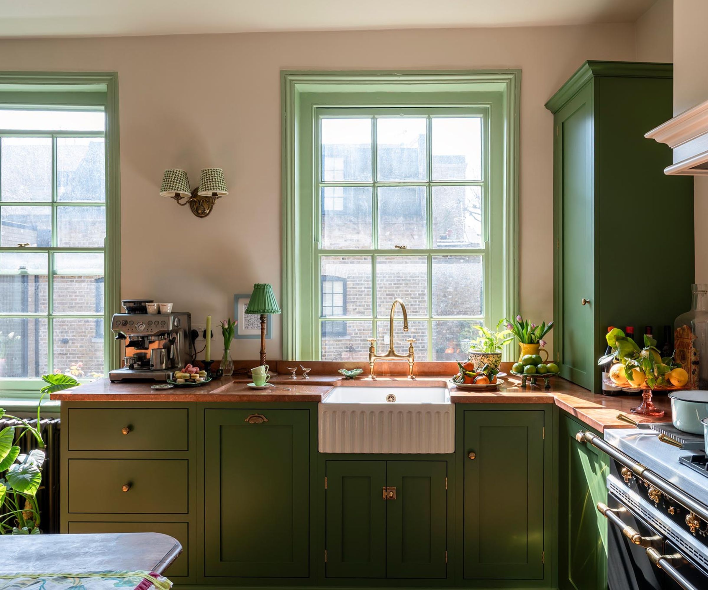 A small kitchen with green cabinets, copper countertops, and large sass windows painted sage green