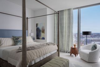 four poster bedroom blue headboard and full height windows with views of city skyline