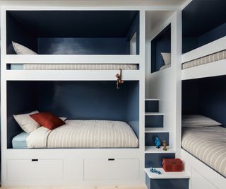 built in quadruple bunk beds with white frames, steps and navy walls behind