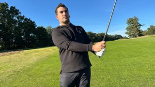 A golfer swings in a Pins & Aces hoodie