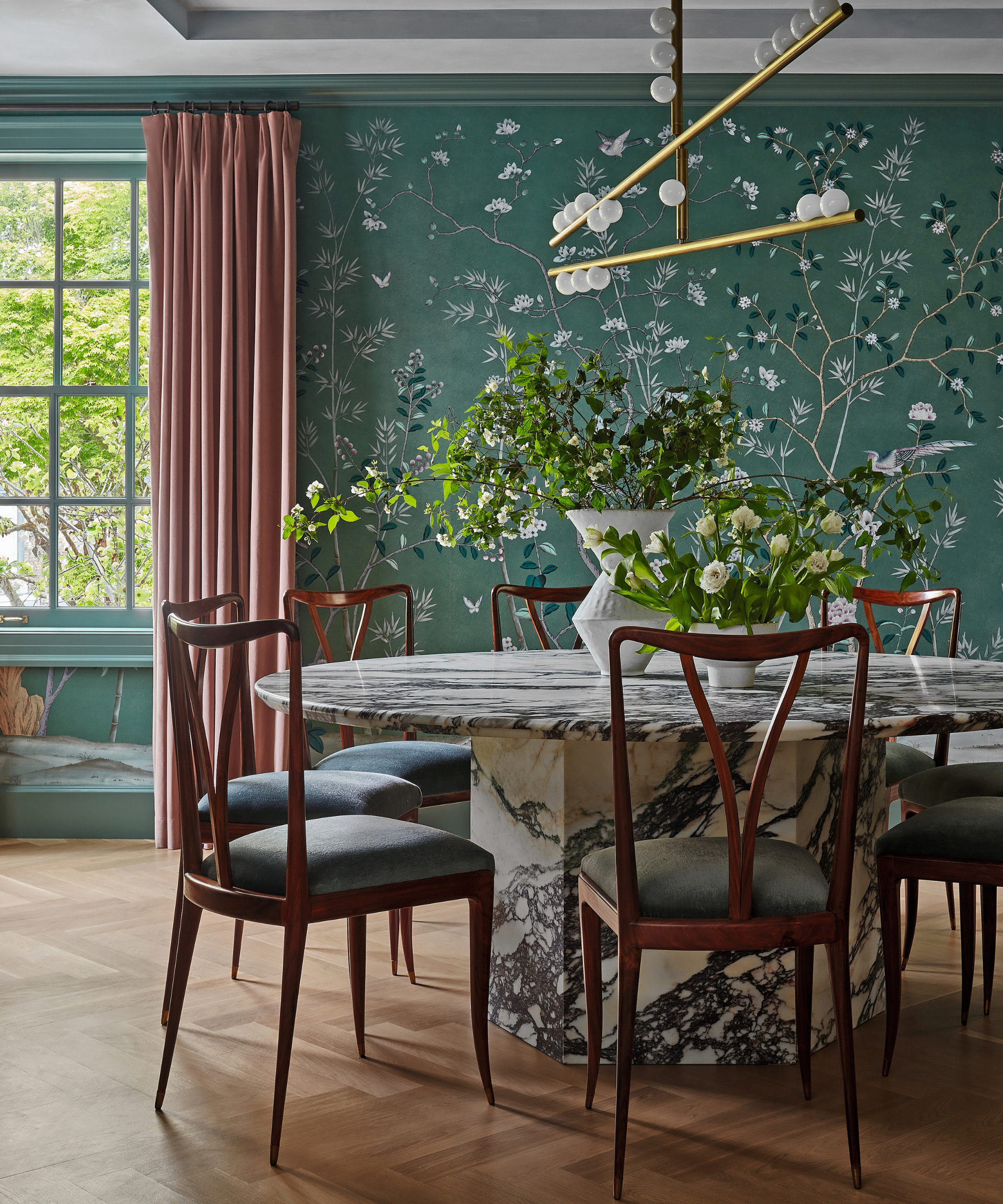 Contemporary dining room with round marble table and wooden chairs and foliage patterned wallpaper and ceiling light