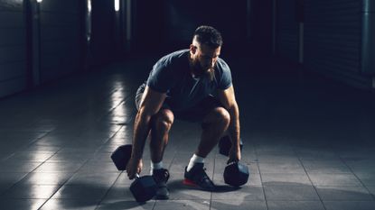 Man bending down in squat position to pick up dumbbells