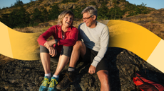 White, straight couple in athletic wear sitting by the side of a mountain laughing