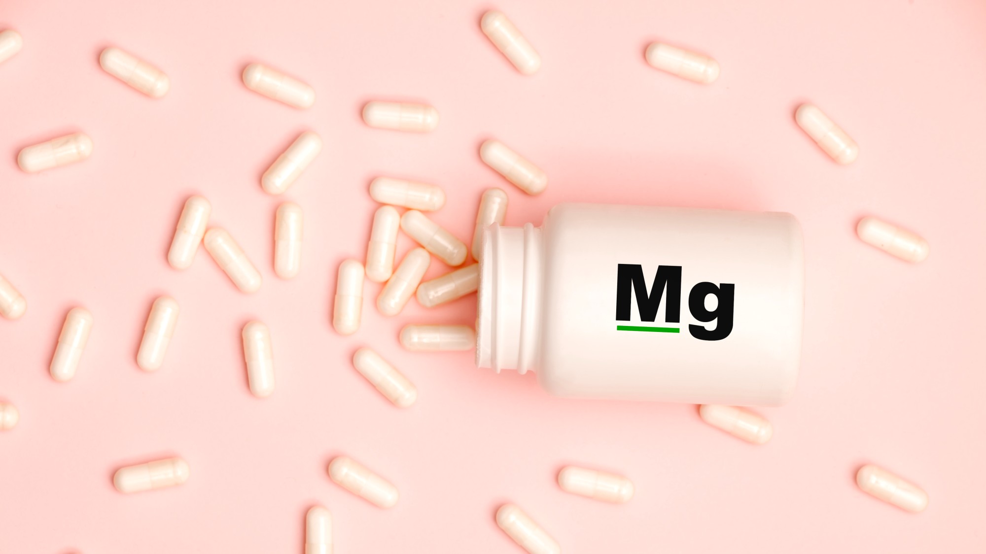 White medicine capsules spilled out of a jar on light Pink background 