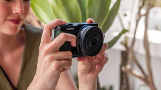 Panasonic Lumix S 26mm f/8 lens attached to a camera and held in a pair of hands