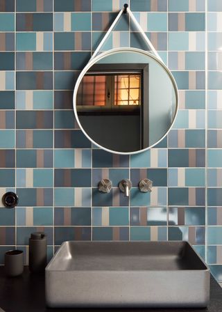 A bathroom with a sink, round mirror and blue checkered wall tiles.