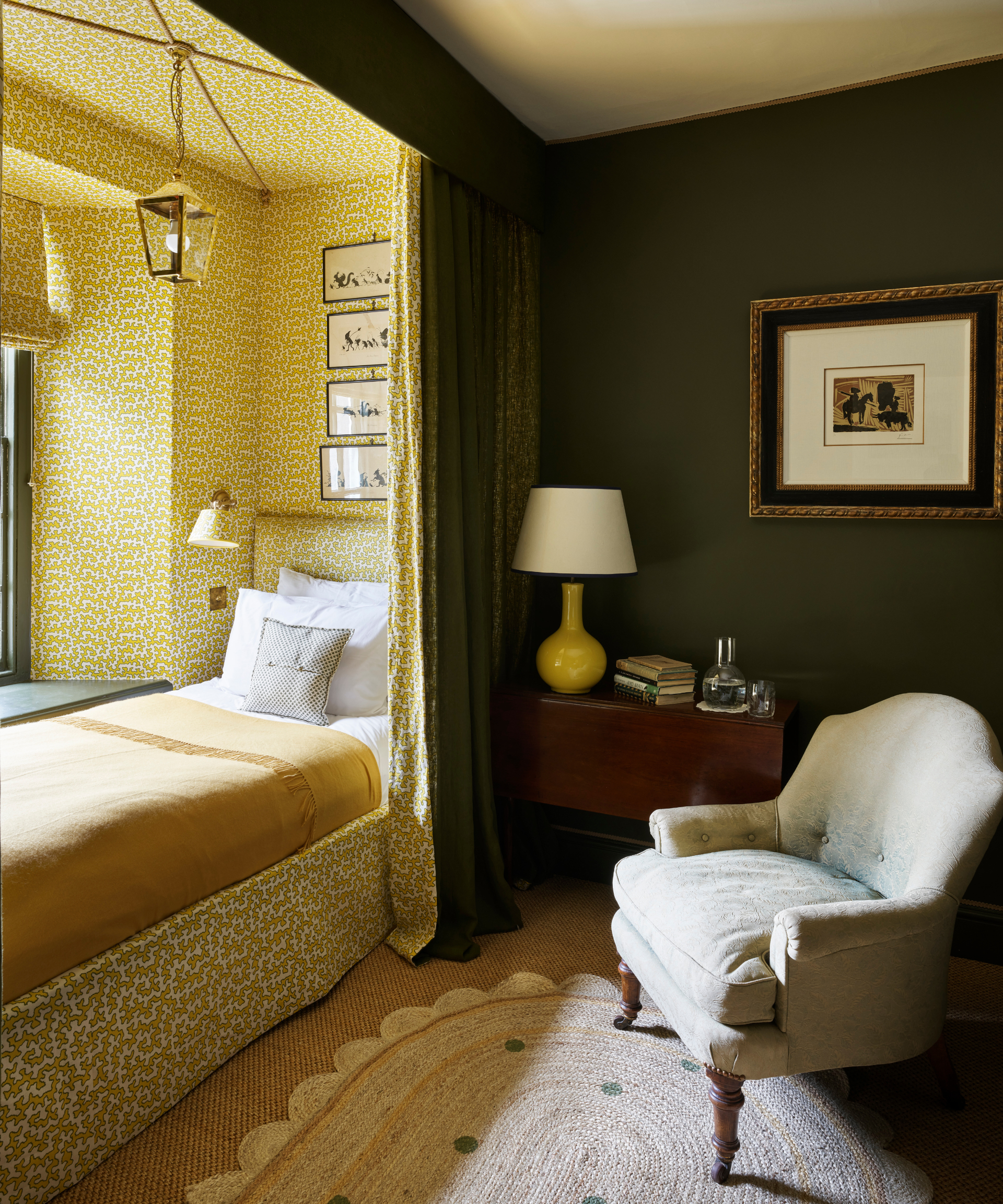 single bed in bedroom nook with curtain to draw across and armchair and rug and sidetable with lamp and patterned wallpaper and matching valance