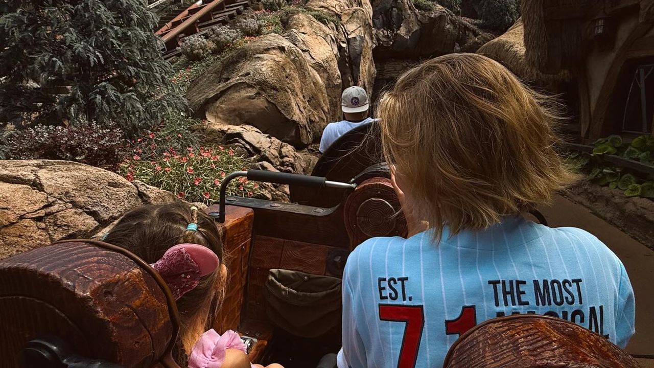 The back of Gigi Hadid wearing a blue jersey and her daughter Khai wearing pink Minnie ears riding a rollercoaster at Disney World