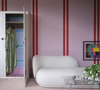 A bedroom with a red and white striped wall with a closet and a boucle day bed