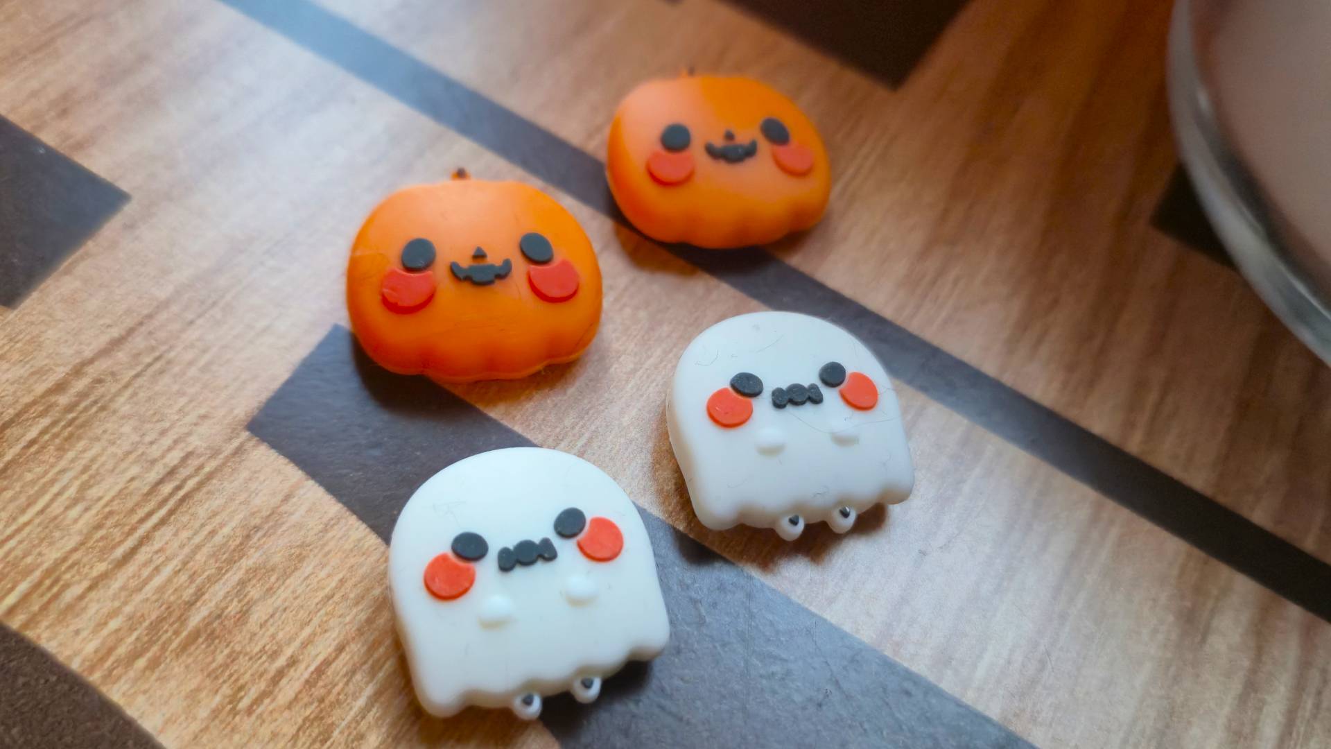 Photo of a set of four thumb grips based on pumpkins and ghosts, sitting on a wooden table.