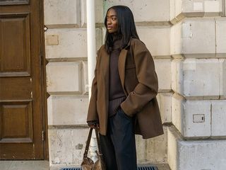 liv wears brown sweater, brown coat, black pants, black tabbis, and brown handbag while posing on the street