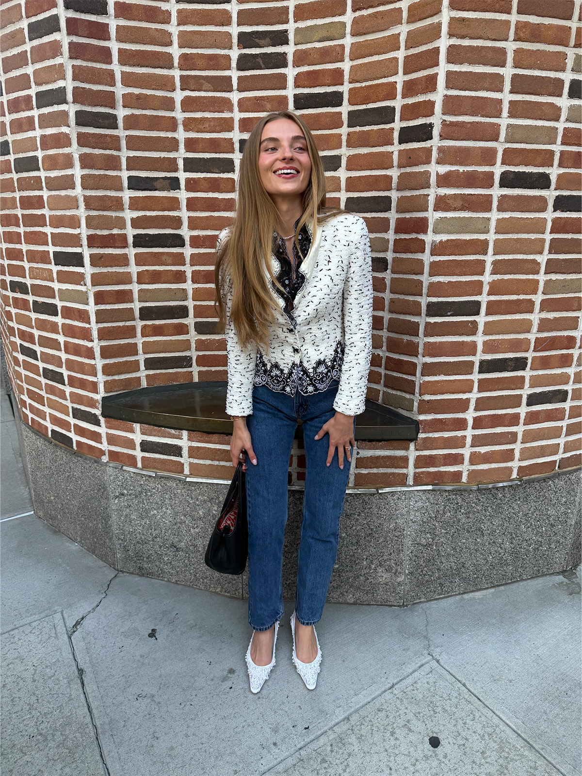 Rae wears a black-and-white jacket, jeans, and white pumps.