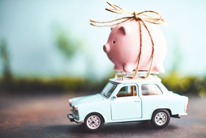 A pink piggy bank is tied to the top of a tiny blue car.