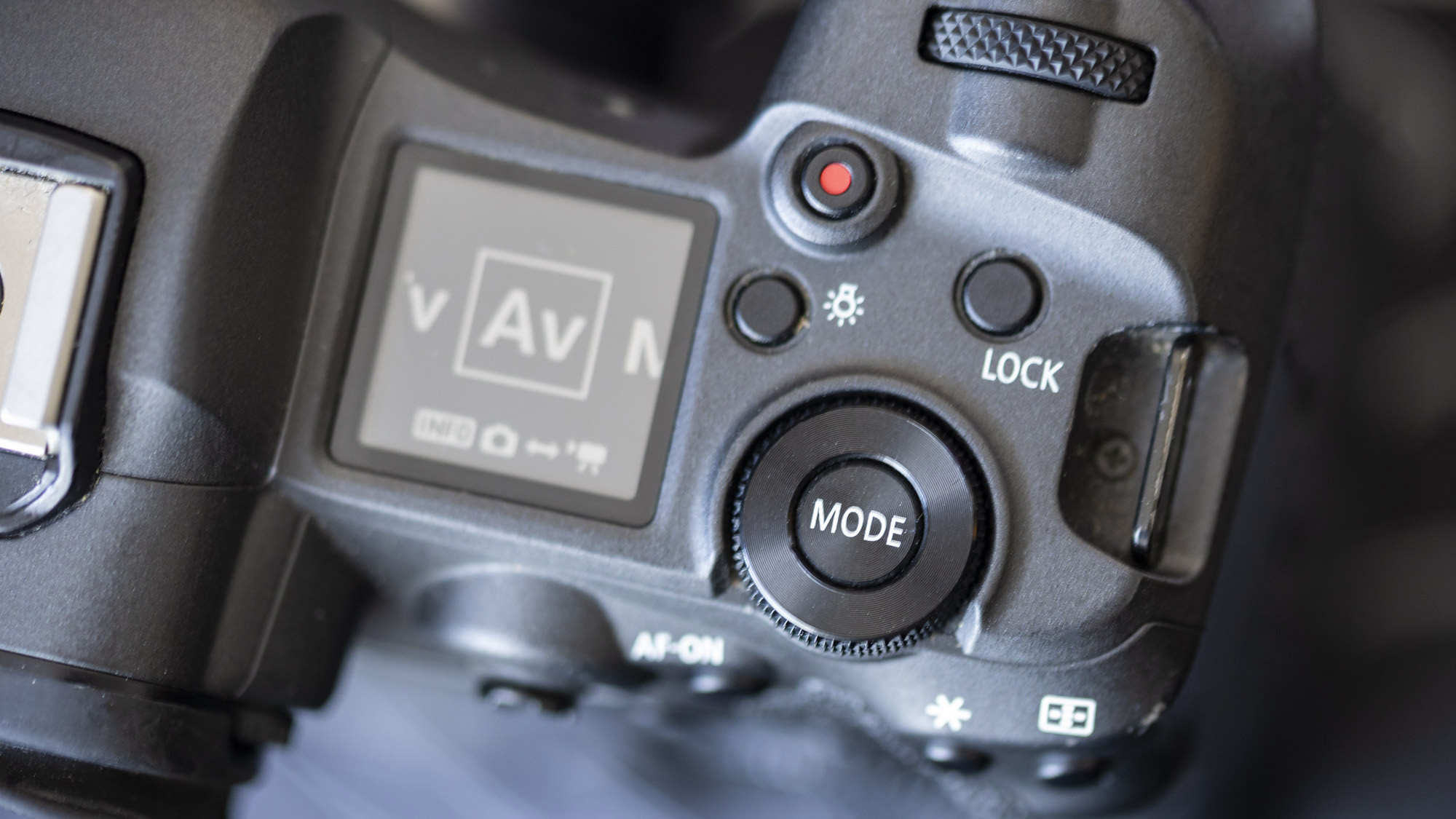 A close-up of the top of Canon EOS R5 showing its Mode button and LCD screen